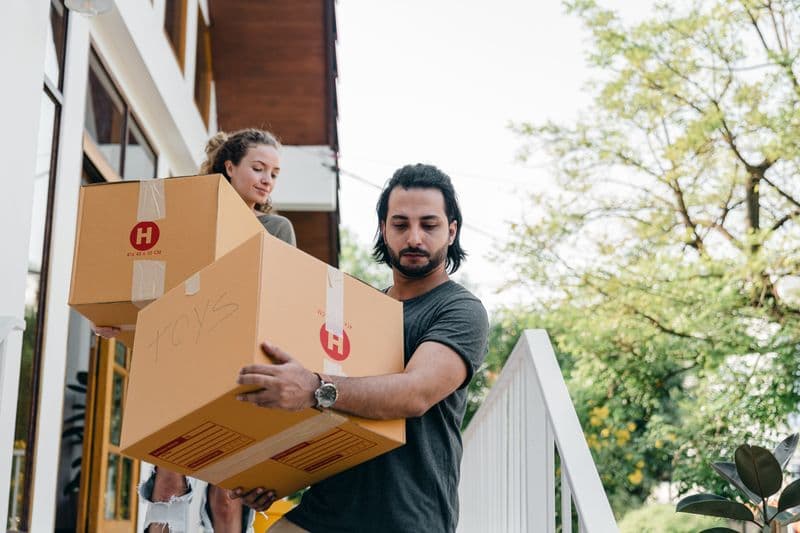 Two people carrying packed boxes out of a home