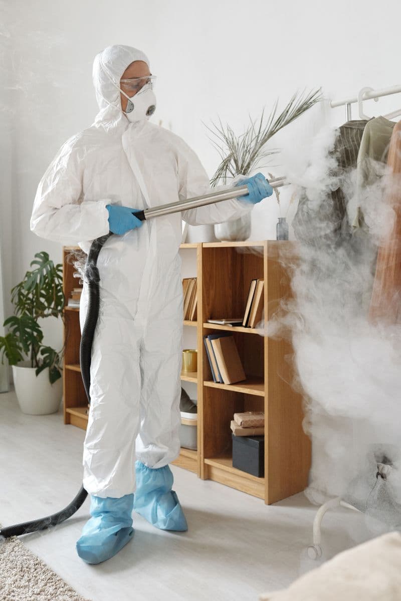 A person in protective clothing using indoor spraying equipment